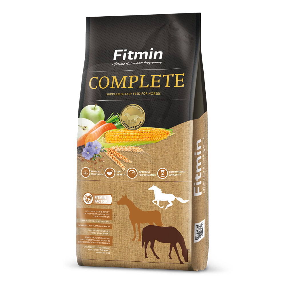 A 15kg bag of Fitmin Horse Complete supplementary feed featuring a dark grey and burlap-textured design. The packaging displays a central graphic of fresh apples, carrots, corn, and flax flowers, alongside horse silhouettes and icons for balanced composition, health, performance, and longevity.