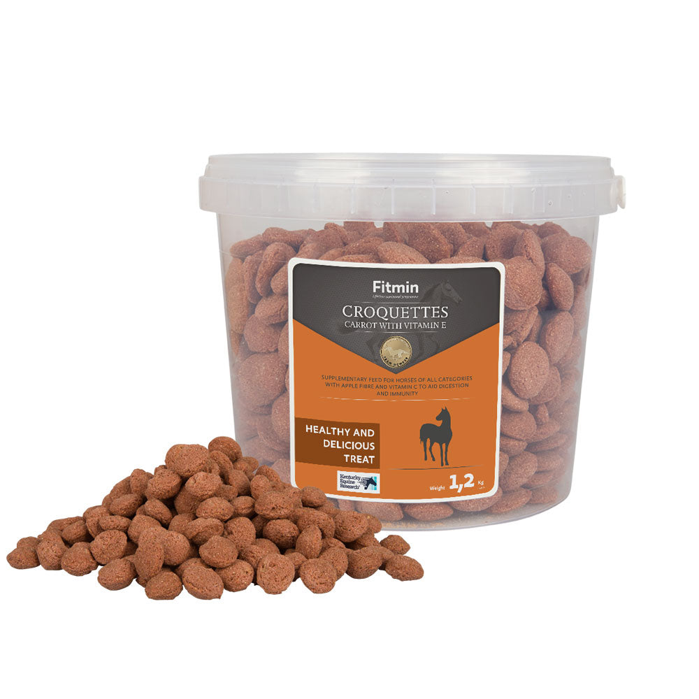 A 1.2kg transparent plastic bucket of Fitmin Horse Croquettes with carrot and Vitamin E, with a small mound of the reddish-brown treats piled in front. The label highlights them as a healthy and delicious treat designed for optimal equine well-being.