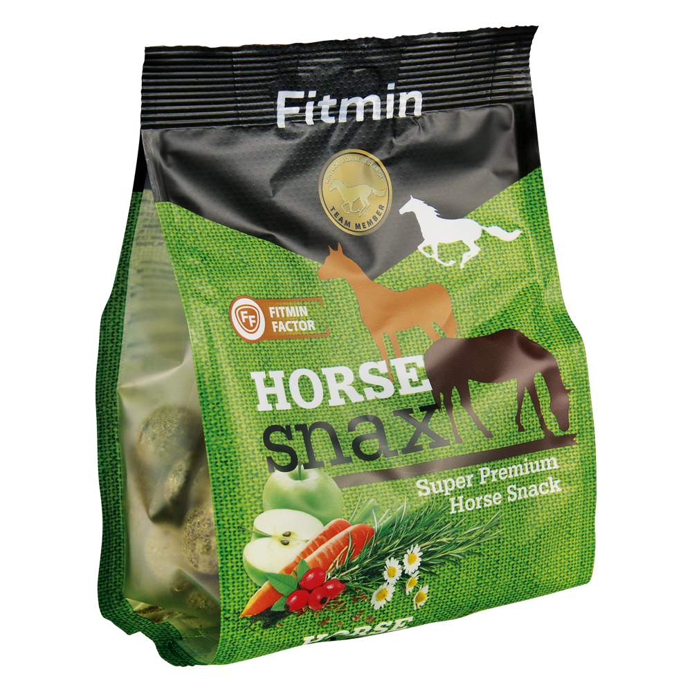 A side-angled view of a green and black stand-up pouch of Fitmin Horse Snax. The packaging features silhouettes of horses and illustrations of natural ingredients including apples, carrots, rosehips, and chamomile. Labeled as a "Super Premium Horse Snack," it includes the Fitmin Faktor and contains visible compressed herbal snack balls through a transparent side panel.